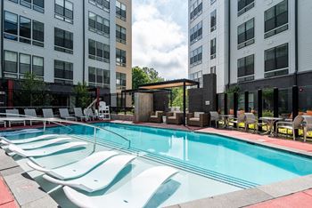 a swimming pool with chairs in front of an apartment building